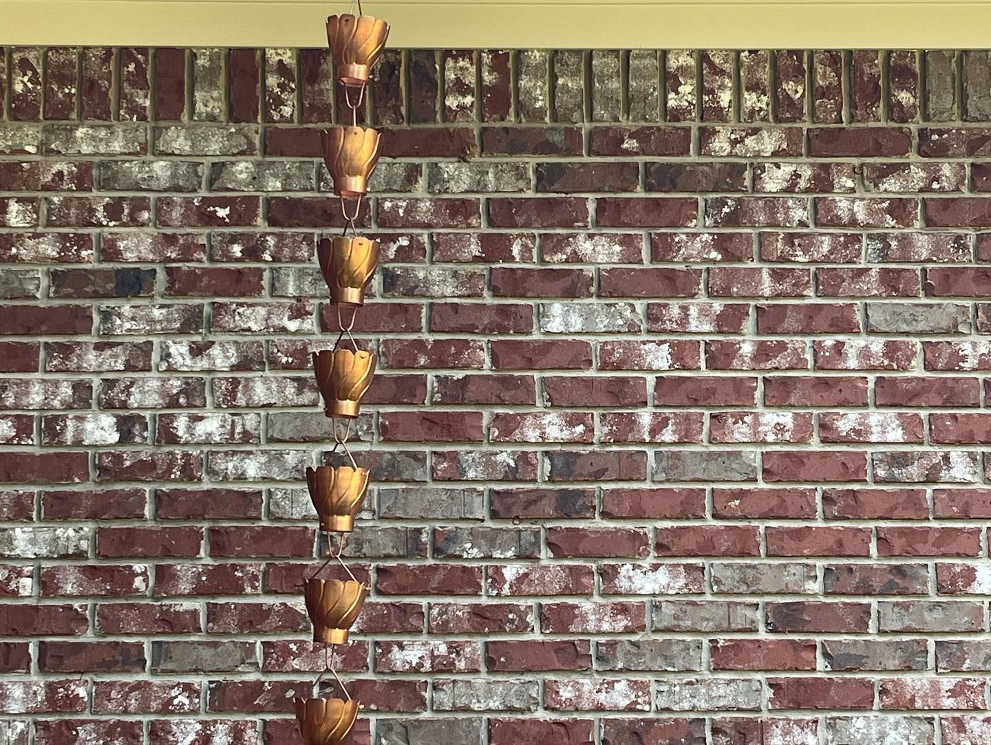 Copper rain chain against a red and gray brick wall.