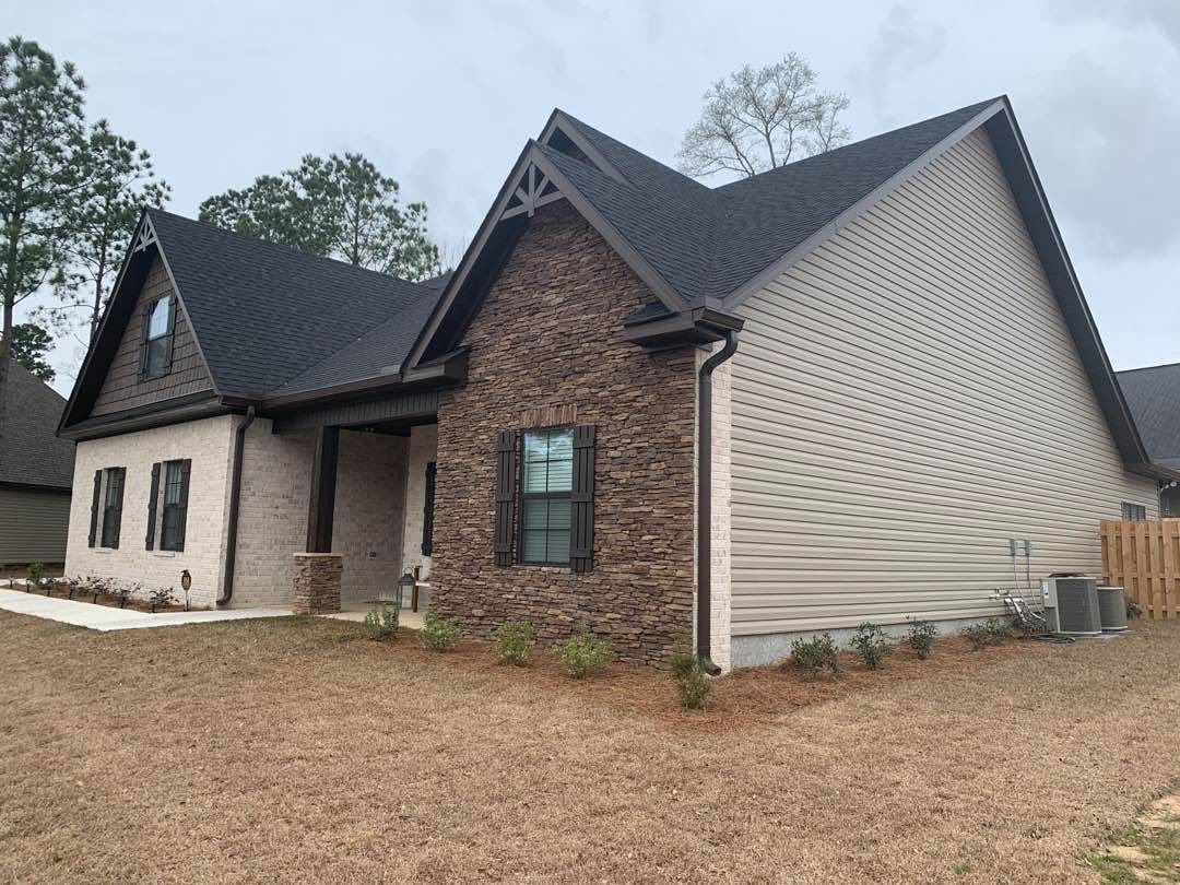 Beige and stone home with dark roof on a cloudy day.