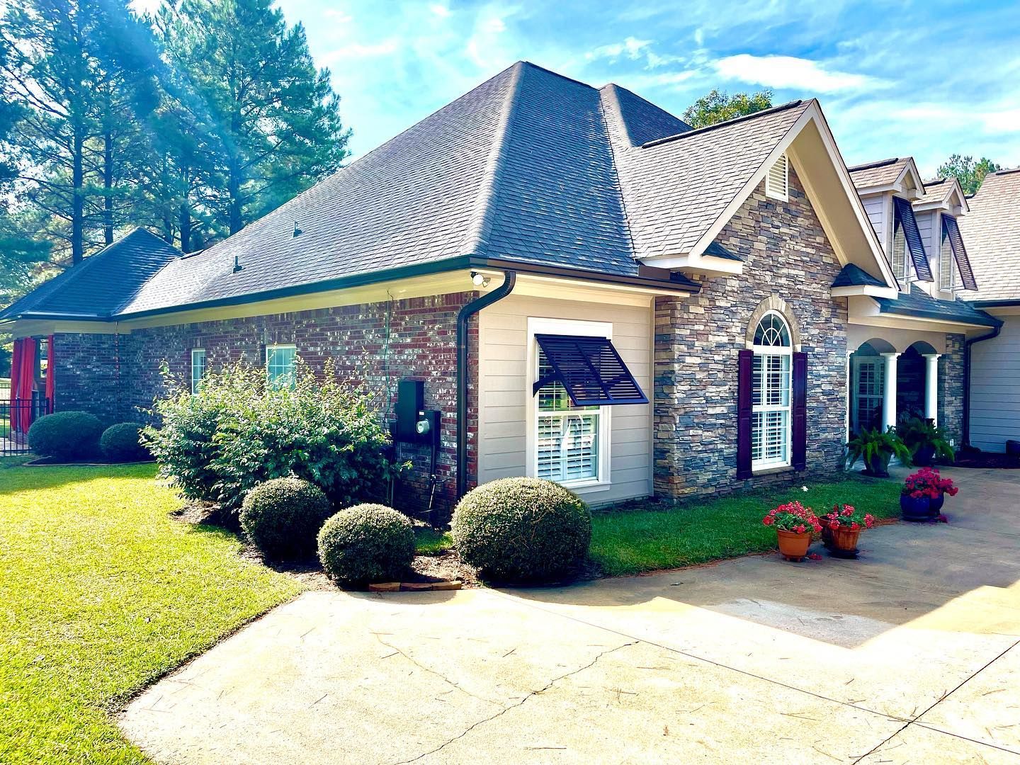 House exterior with stone and brick facade, gray roof, lawn, and driveway.