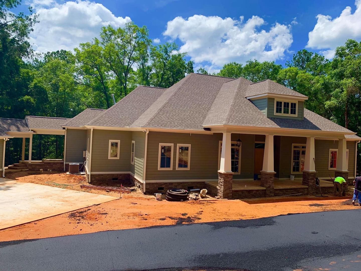 Newly constructed house with gray siding, brown roof, and blue accents, set against a backdrop of trees and blue sky.