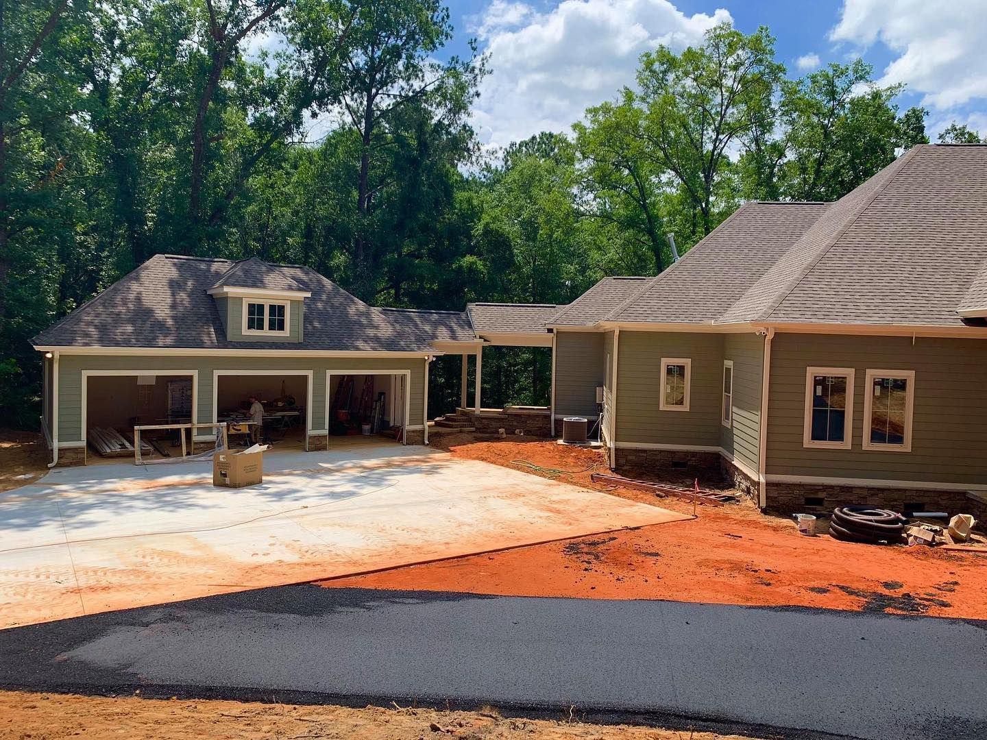 New construction house with attached garage, green siding, gray roof, and red dirt driveway.
