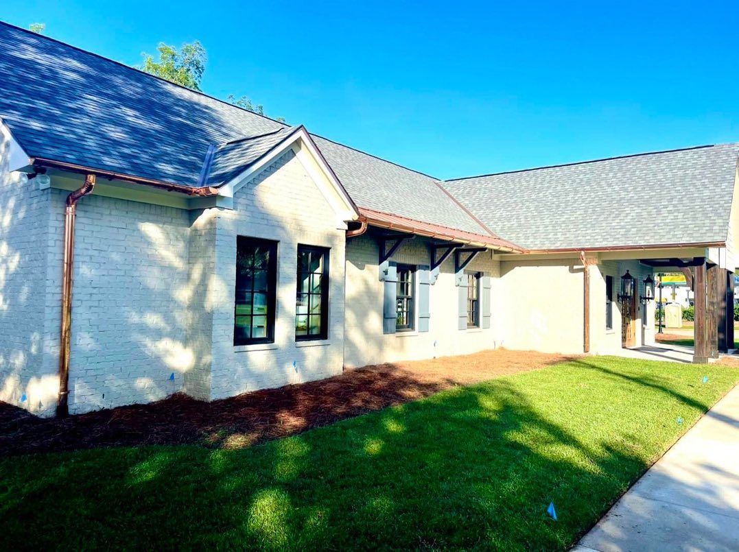 White brick building with dark windows, copper gutters, and green lawn.