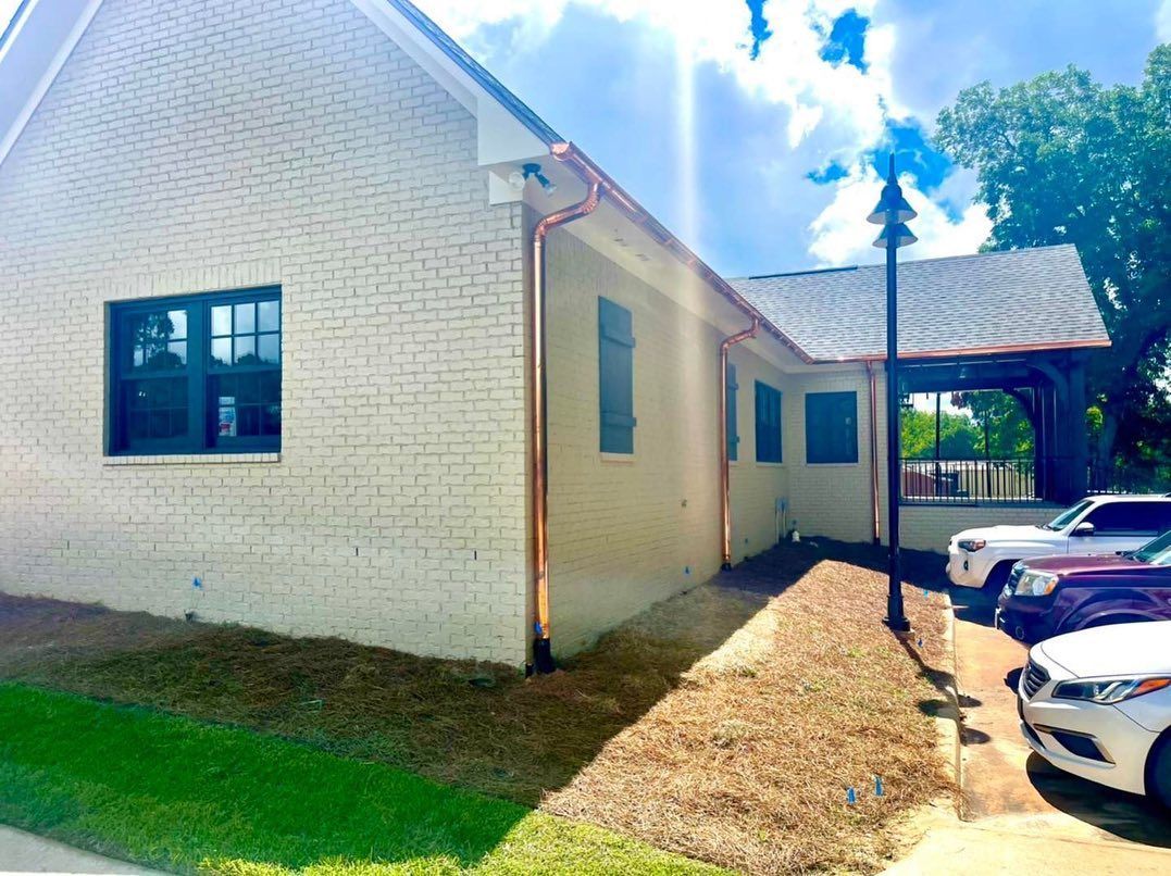 Exterior view of a light brick building with copper gutters, a black window, and a covered patio area.