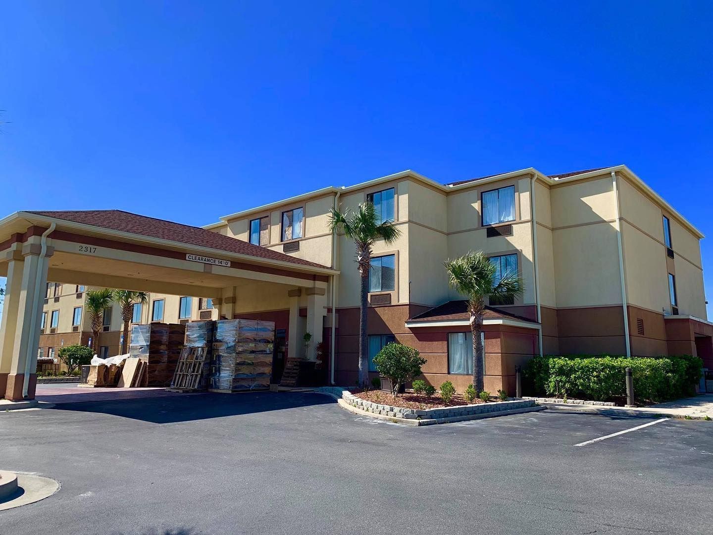 Beige hotel building with a brown roof and trim under a bright blue sky.