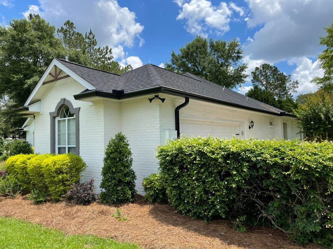 White brick building with black roof and green landscaping under a blue sky.