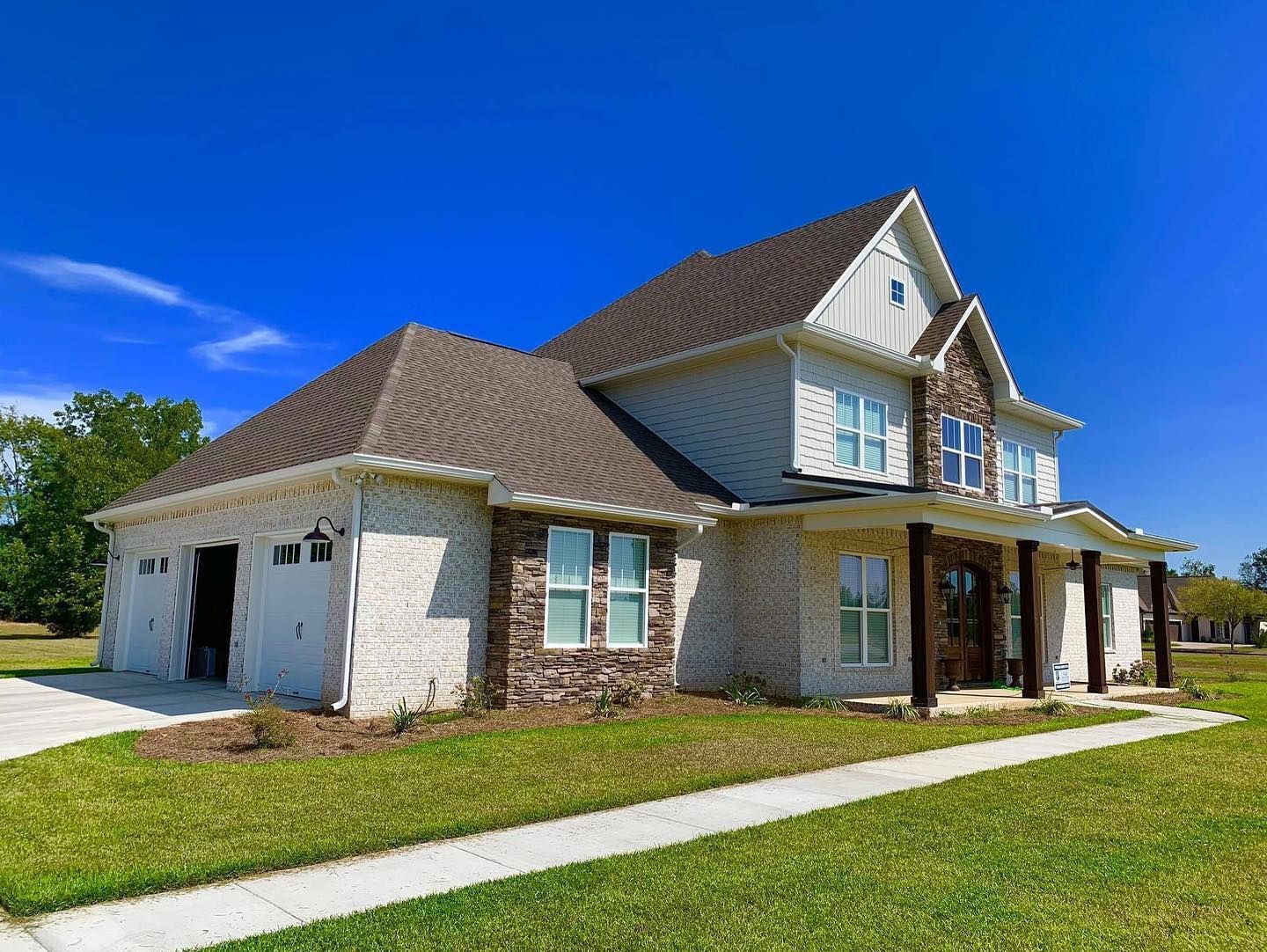 Two-story house with a white brick exterior, brown roof, and a green lawn under a blue sky.