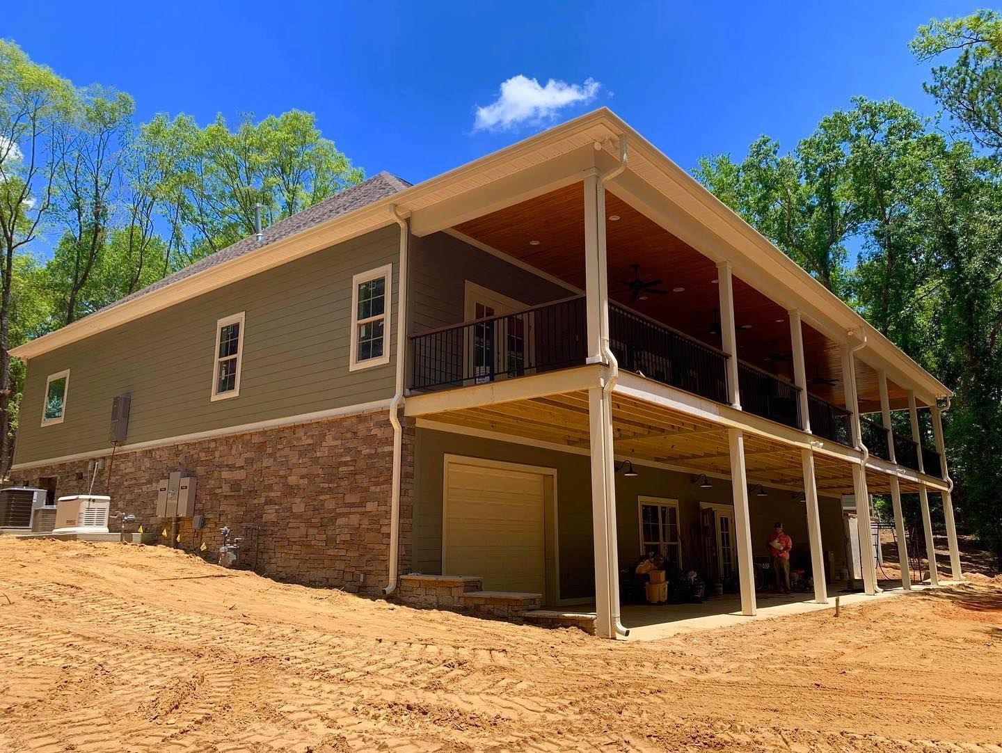 Two-story house with stone foundation, green siding, and wrap-around porch in a wooded setting.