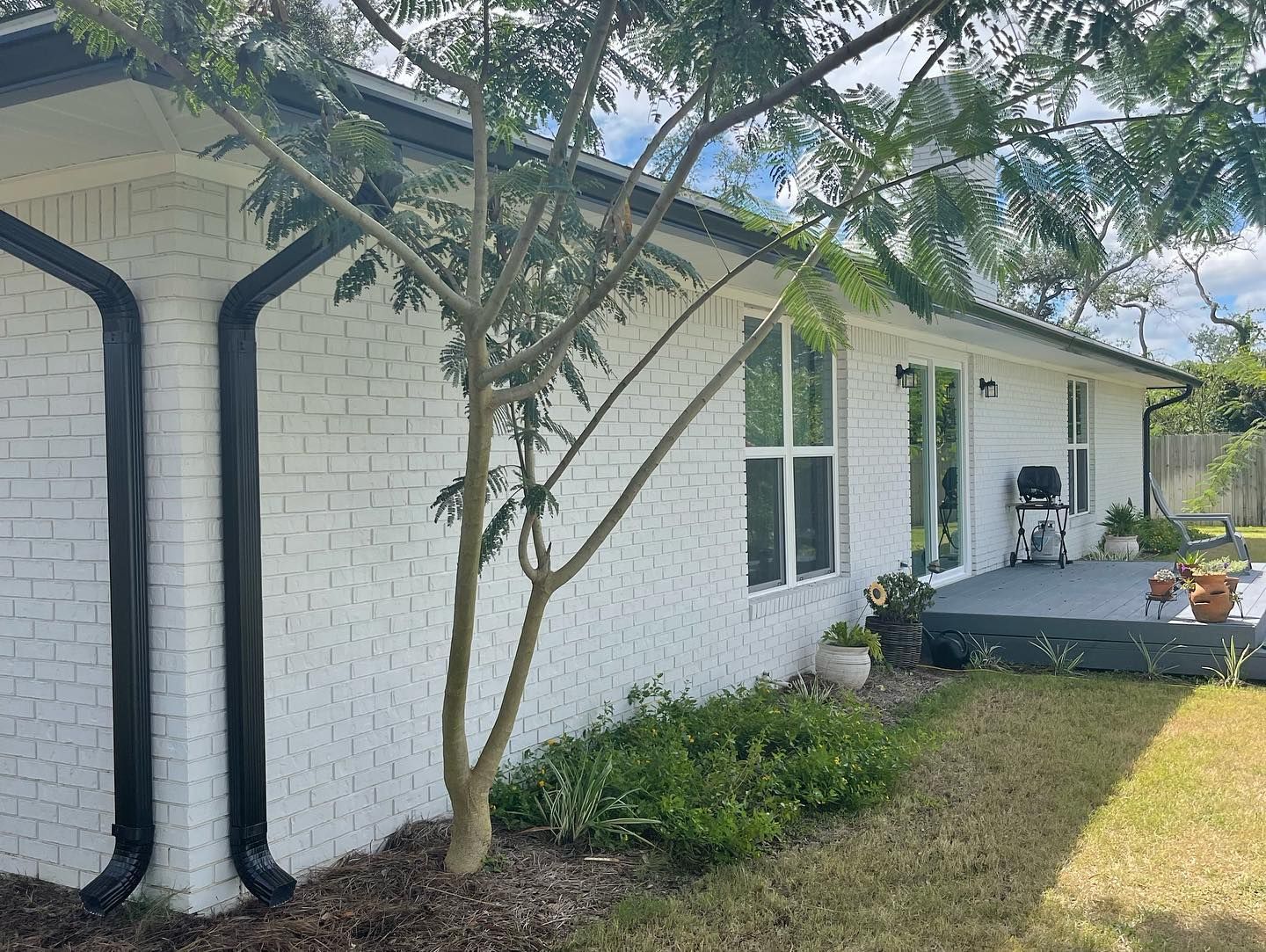 White-painted brick house with black gutters and trim. Windows and a small patio are visible.