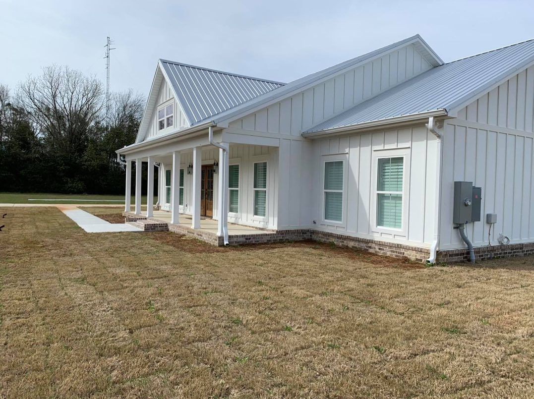 White farmhouse with metal roof, porch, and bare lawn.