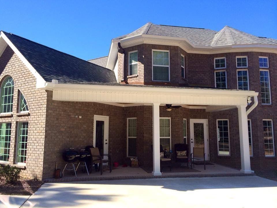 Brick home with a covered patio, white columns, and windows, against a blue sky.