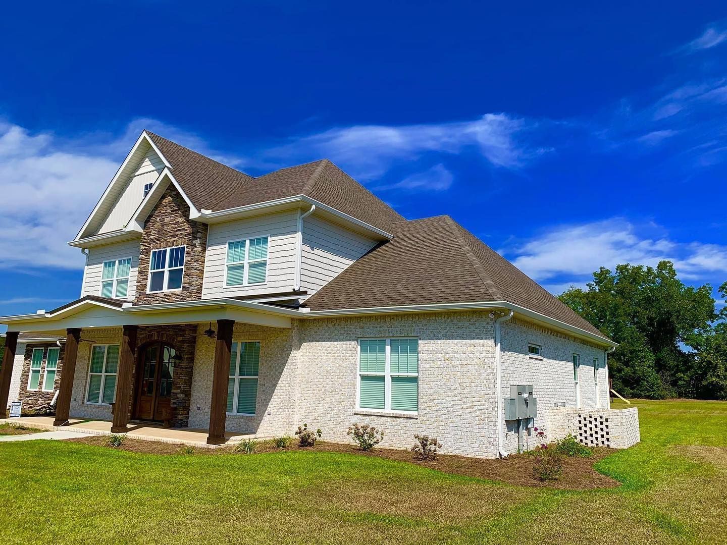 Two-story white brick house with brown roof and wooden porch under a blue sky.