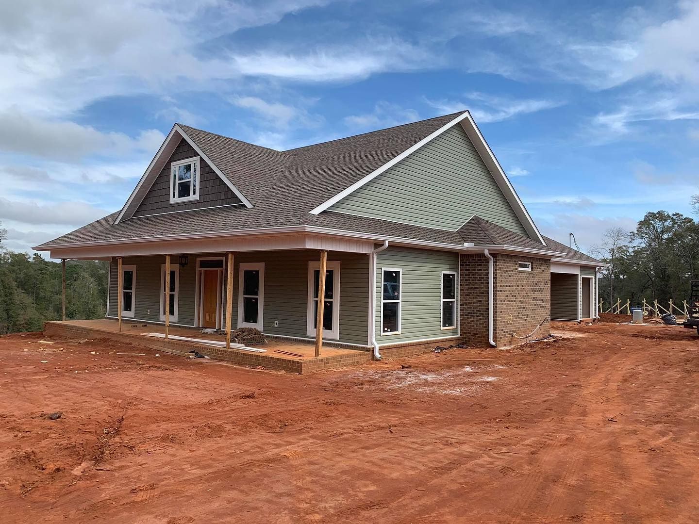 New house under construction with green siding, brown roof, and red dirt ground.