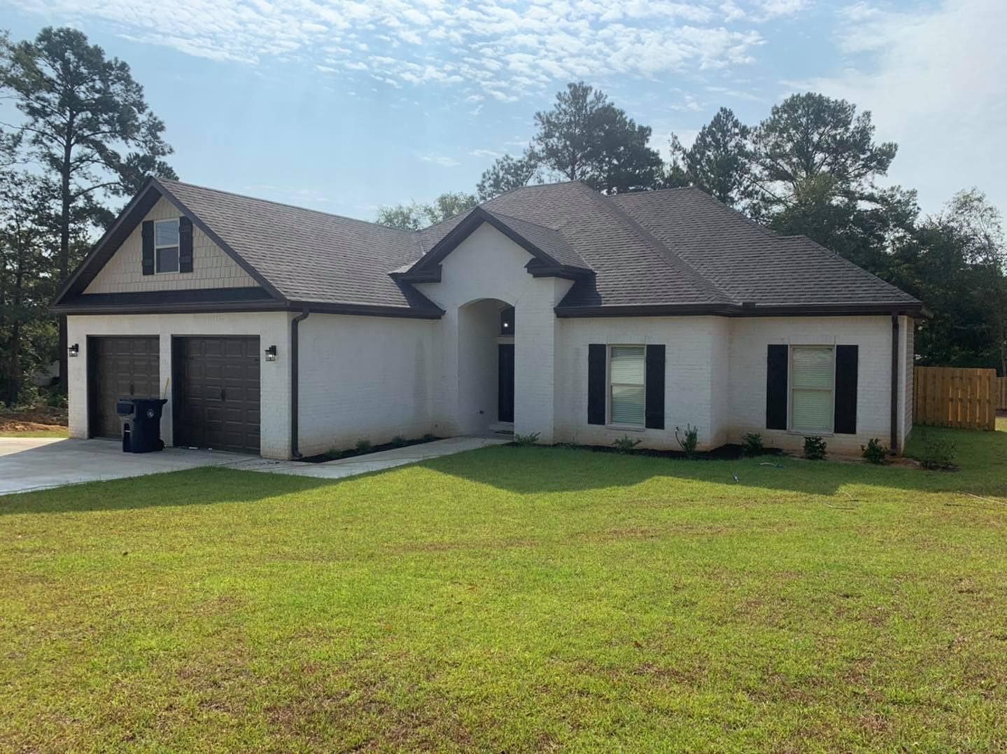 White house with dark roof and trim, green lawn, two-car garage, and blue sky.