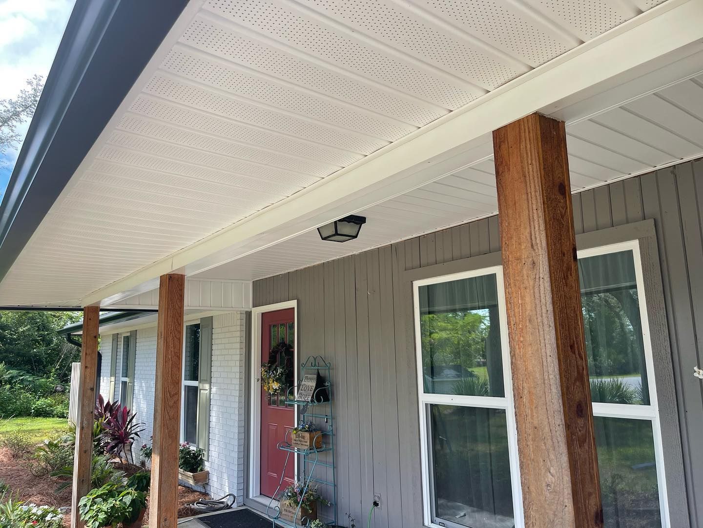 Porch with white patterned ceiling, wood posts, gray siding, and red door.