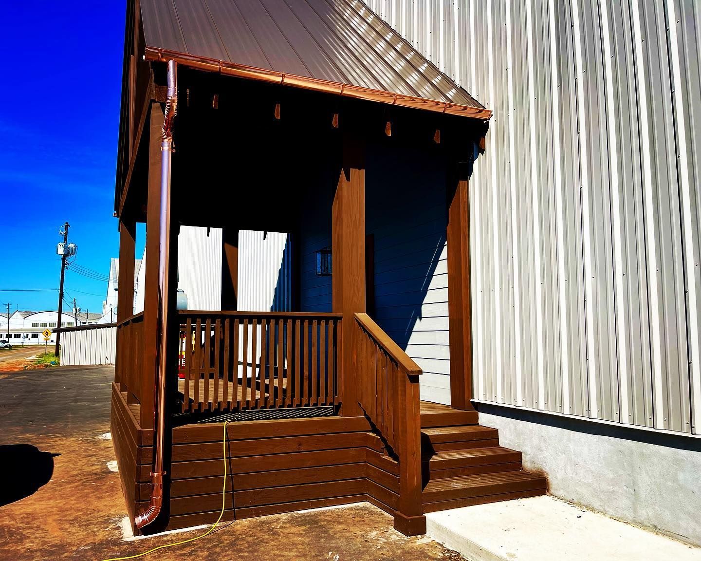 Brown wooden porch with metal roof and stairs next to a building with vertical siding.