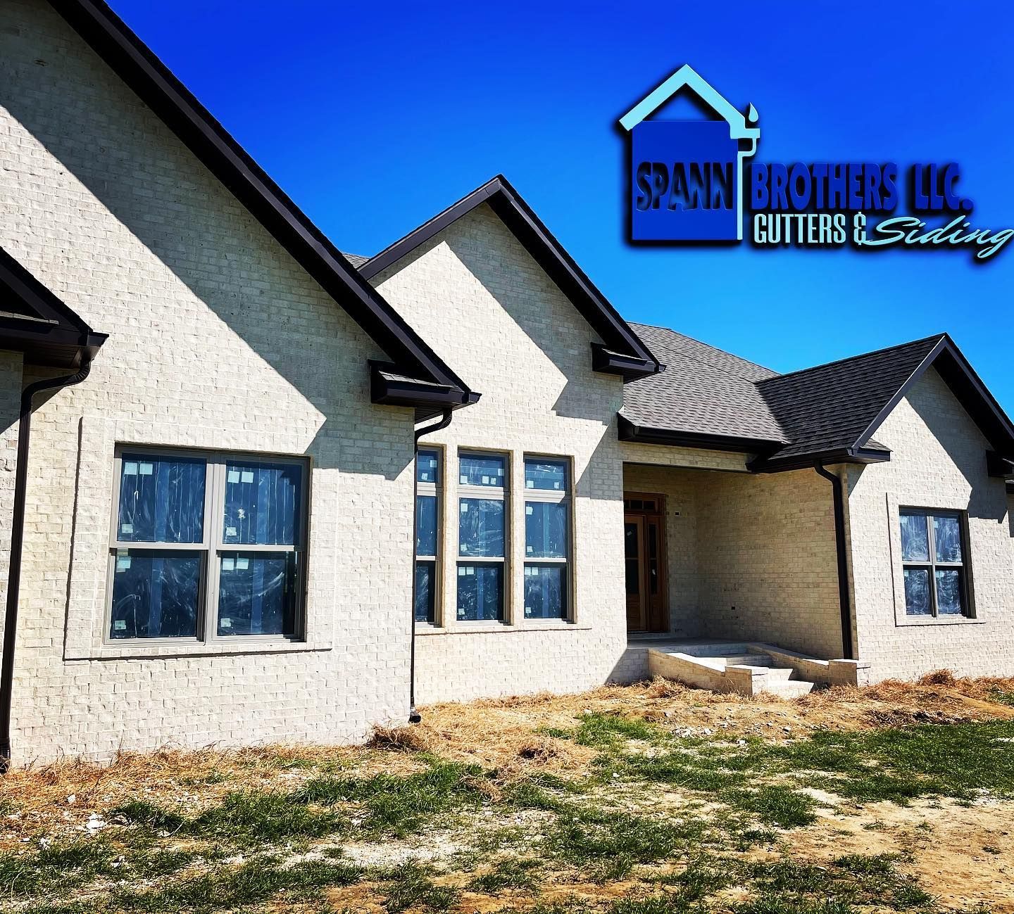 Beige stucco house with dark trim, windows covered in blue film, Spahn Brothers LLC logo.