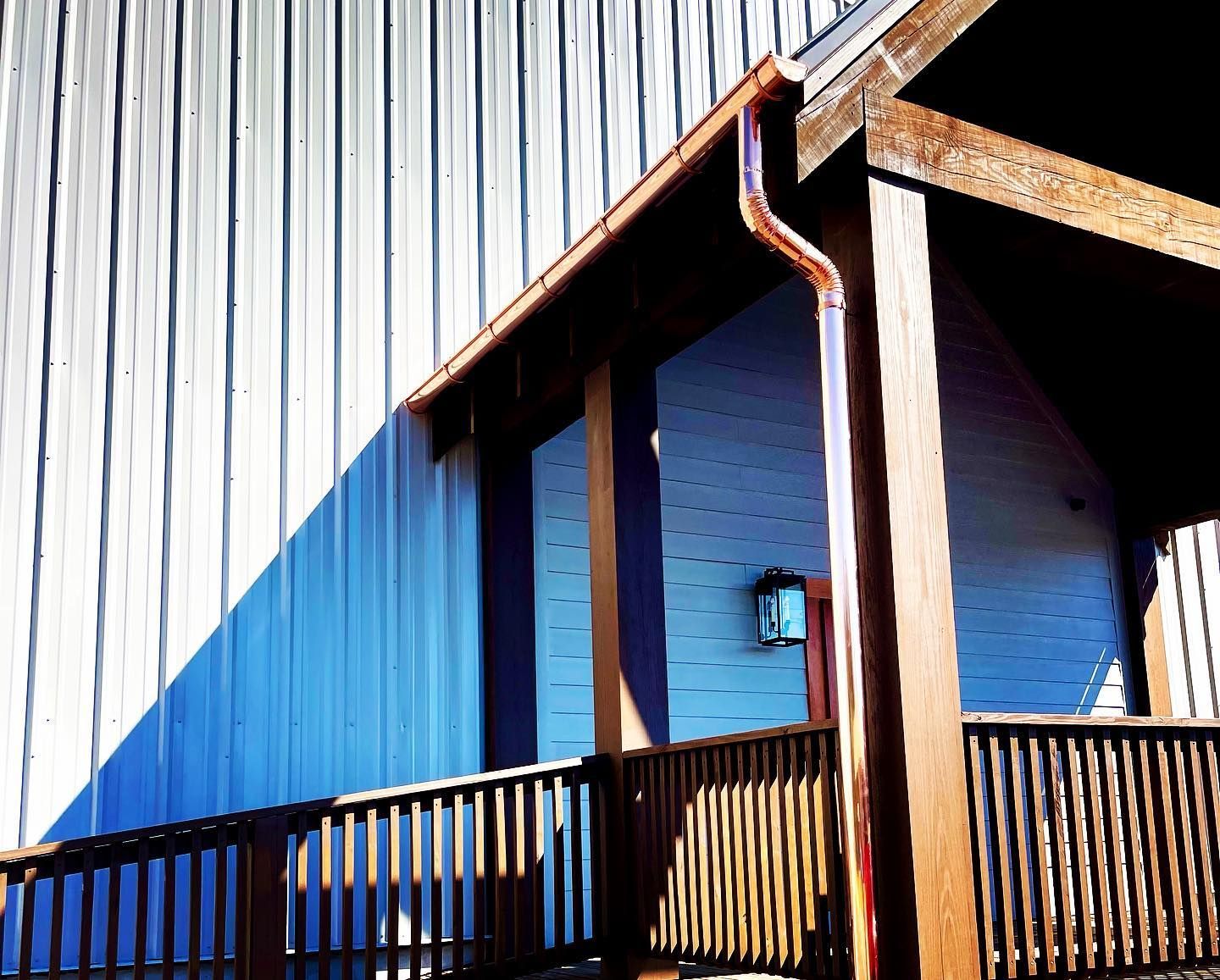 Copper gutters on a wooden porch roof beside a building with vertical metal siding.