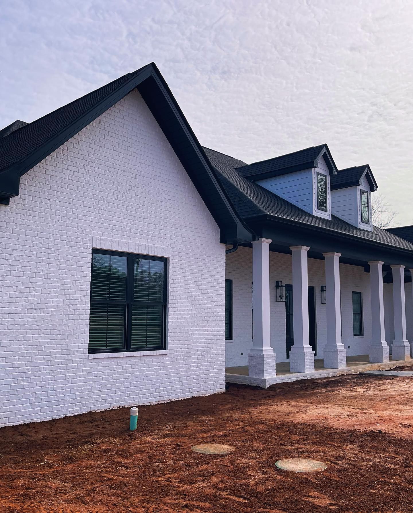 White brick house with black roof, columns, and windows; built on a brown dirt lot.
