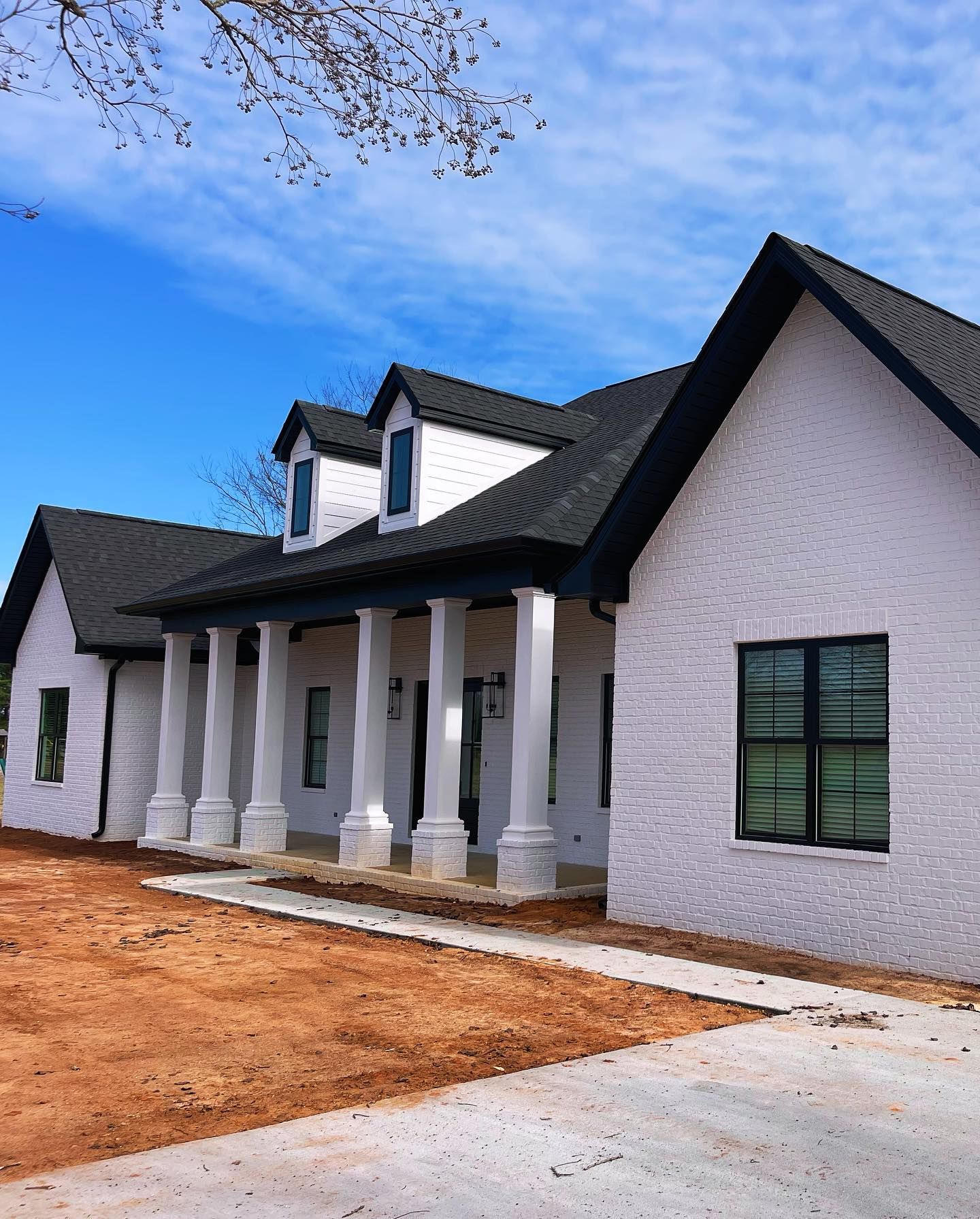 White brick house with black roof and trim, large columns, under a blue sky.