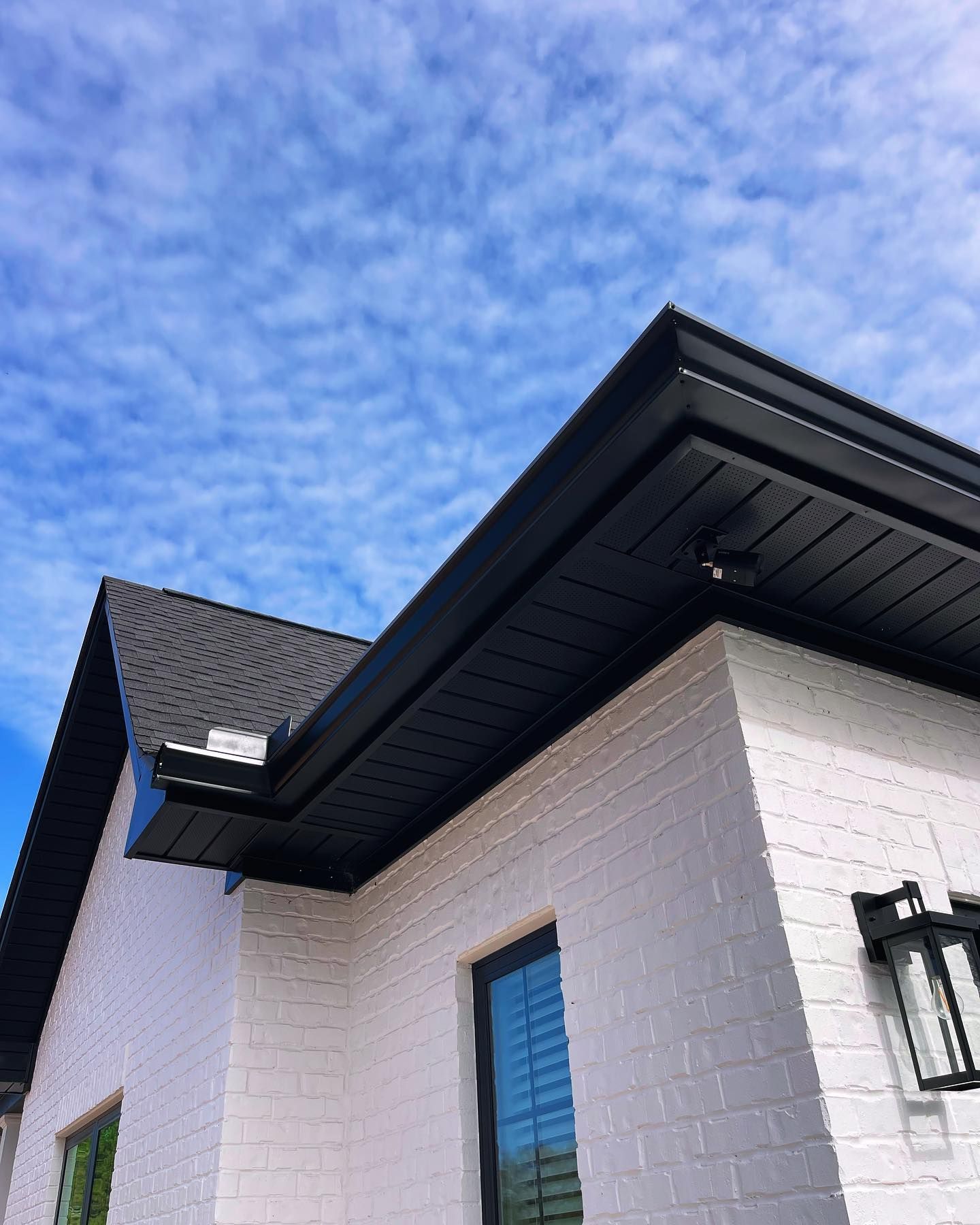 Black roof and trim on a white brick house against a blue sky with fluffy clouds.