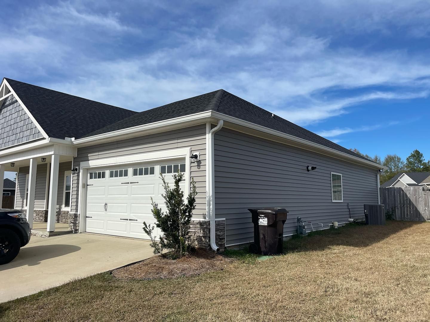 Garage and house exterior with gray siding, black roof, and a blue sky.