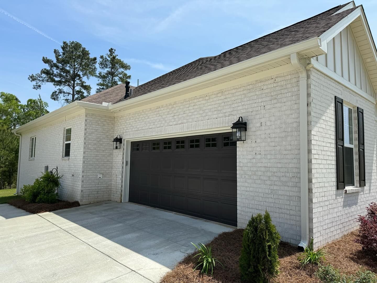 Exterior of a house with a gray garage door, white brick, and a concrete driveway.