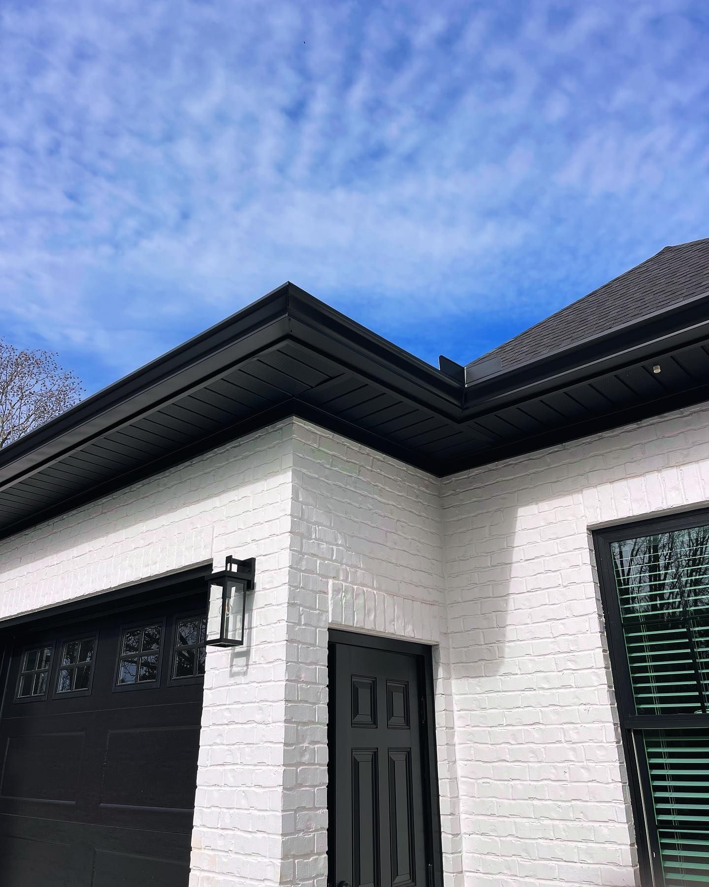 White brick building with black trim, door, and garage door under a blue sky.