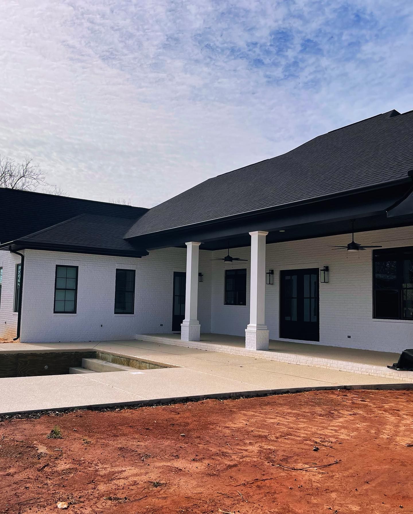 White brick house with black roof, outdoor patio, and two white pillars.