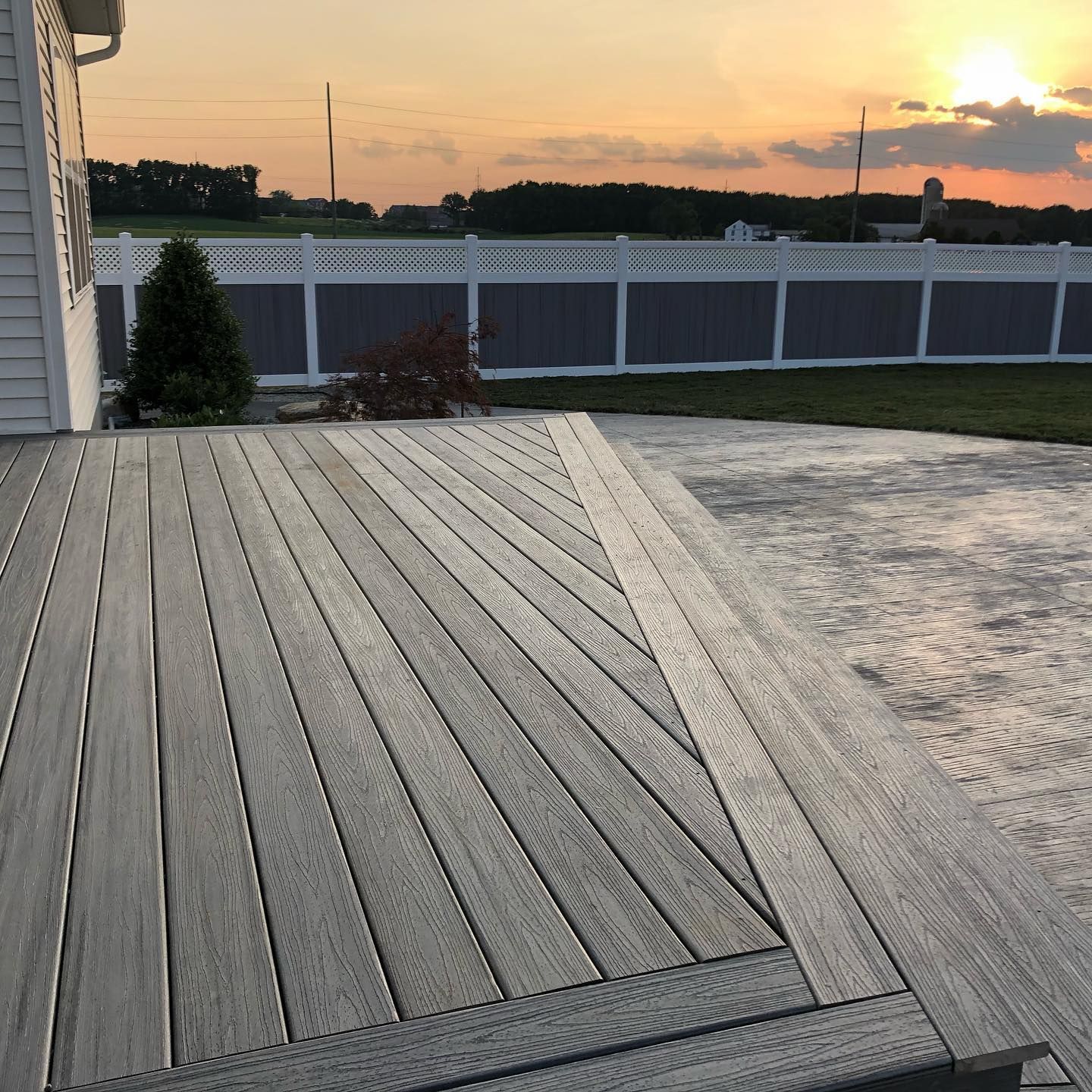 Gray deck with angled design, concrete patio, white and gray fence at sunset.