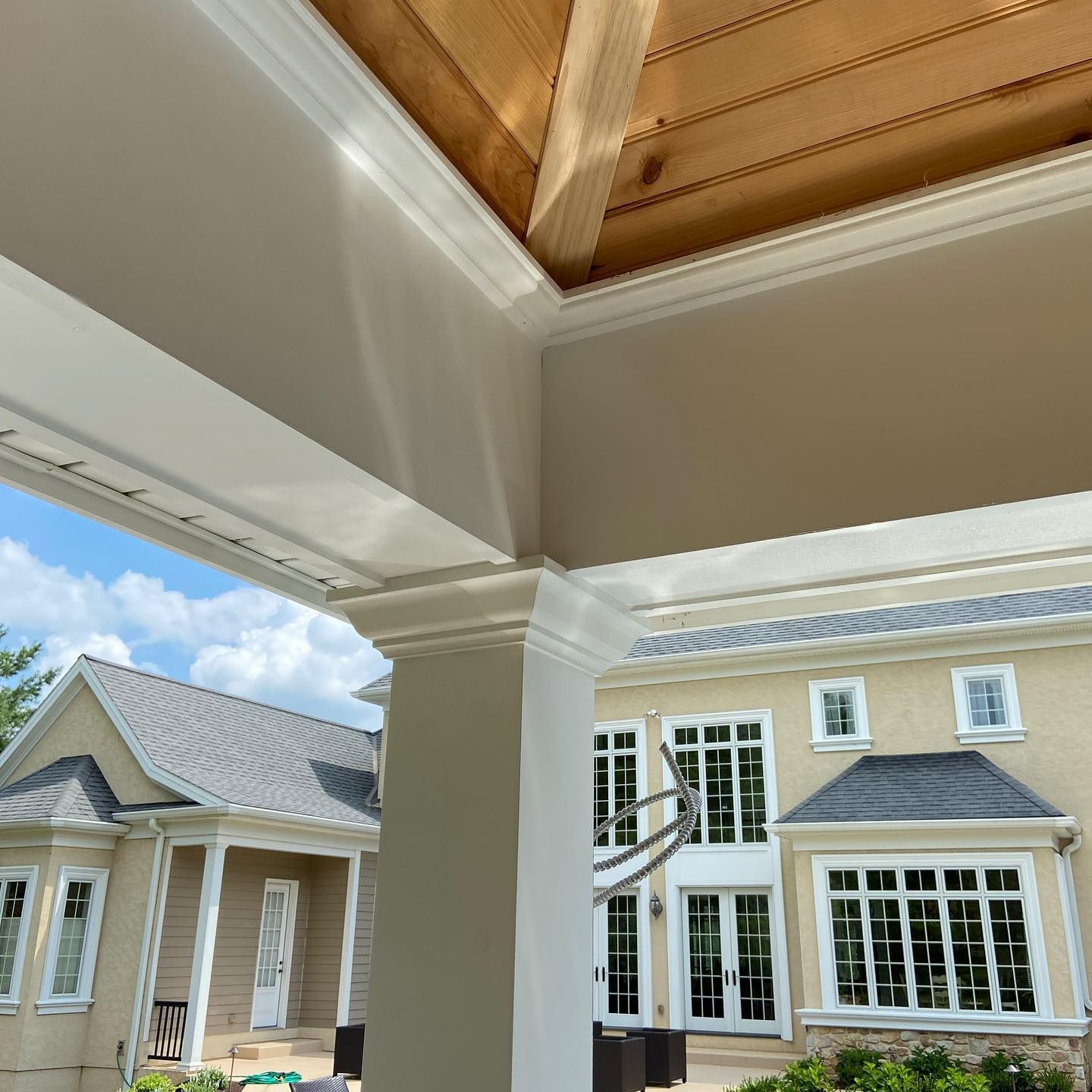 Beige columns and trim on a porch, overlooking two-story beige house with many windows. Blue sky.