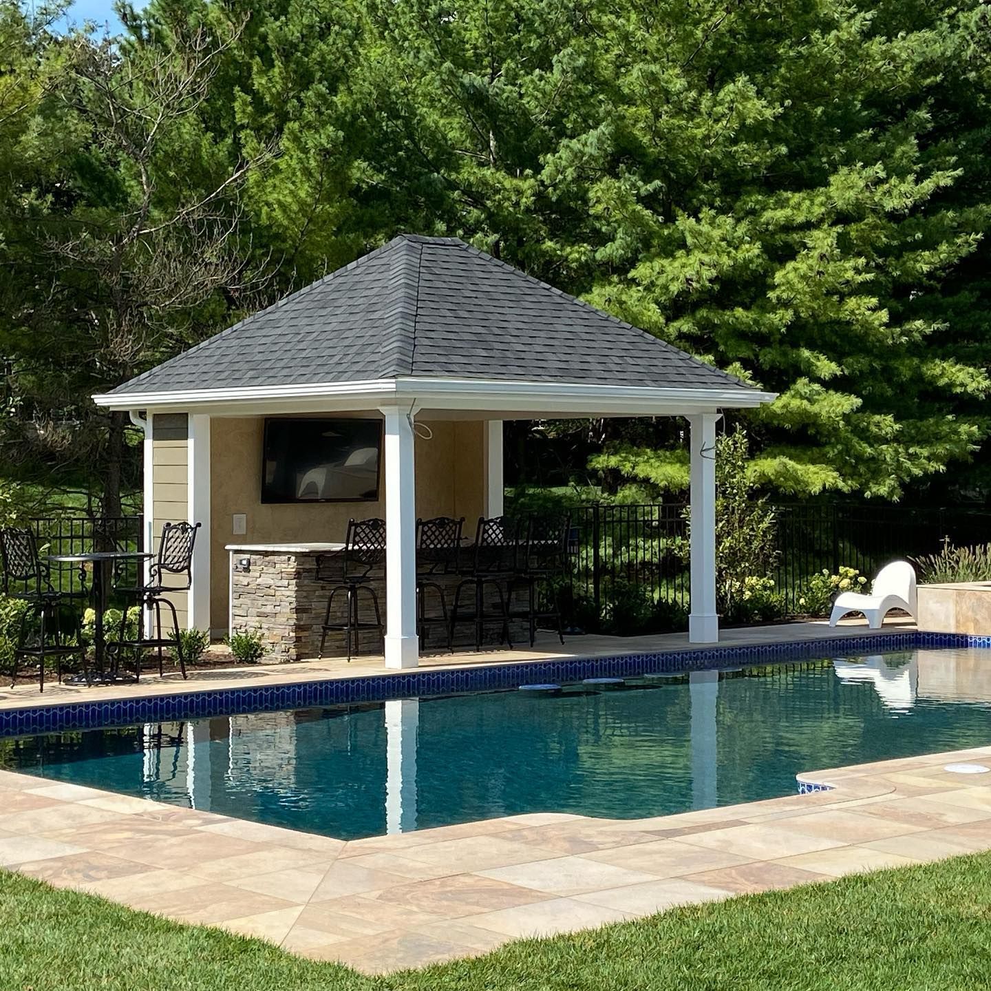 Poolside cabana with a bar, television, and seating, reflected in the water.