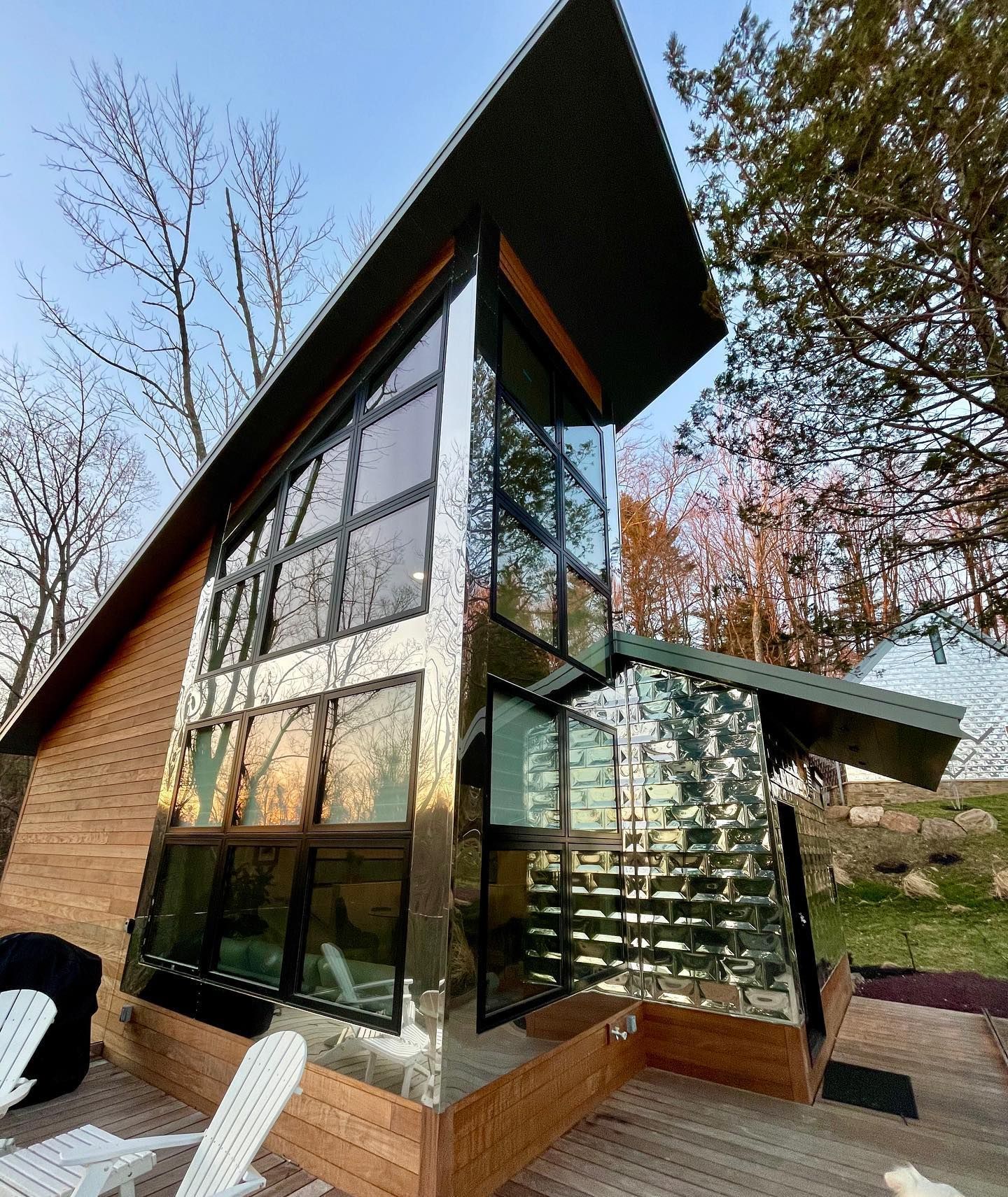 Modern cabin with glass windows and mirrored exterior. Set on a wooden deck, surrounded by trees.