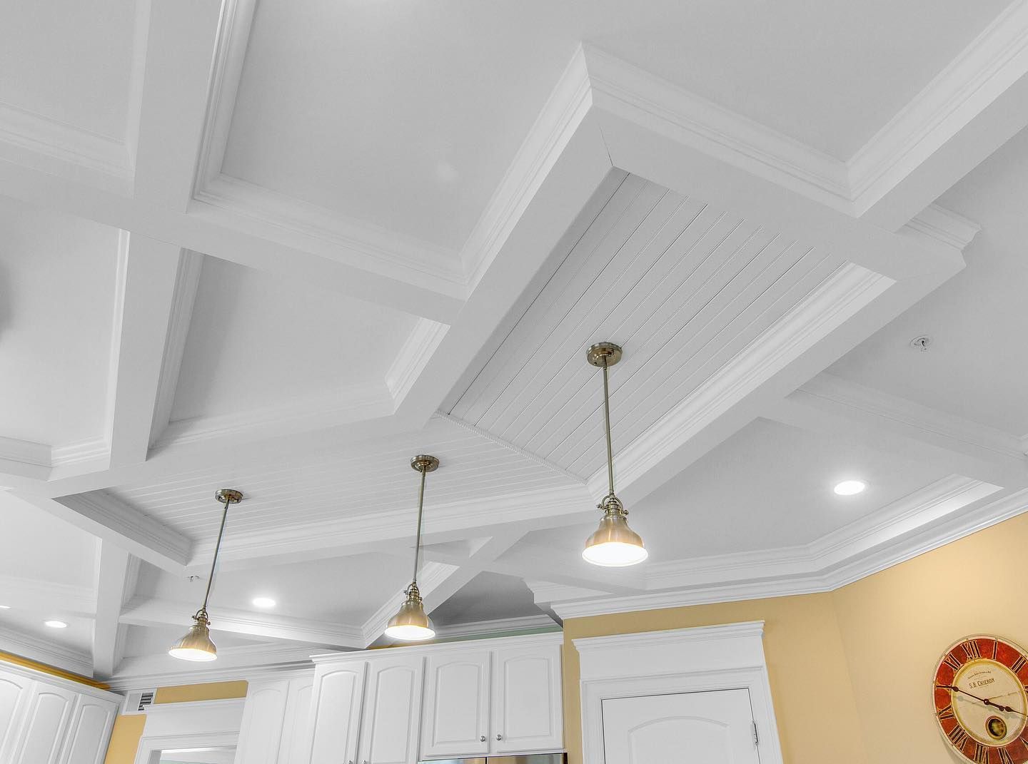 White coffered kitchen ceiling with three pendant lights and recessed lighting.