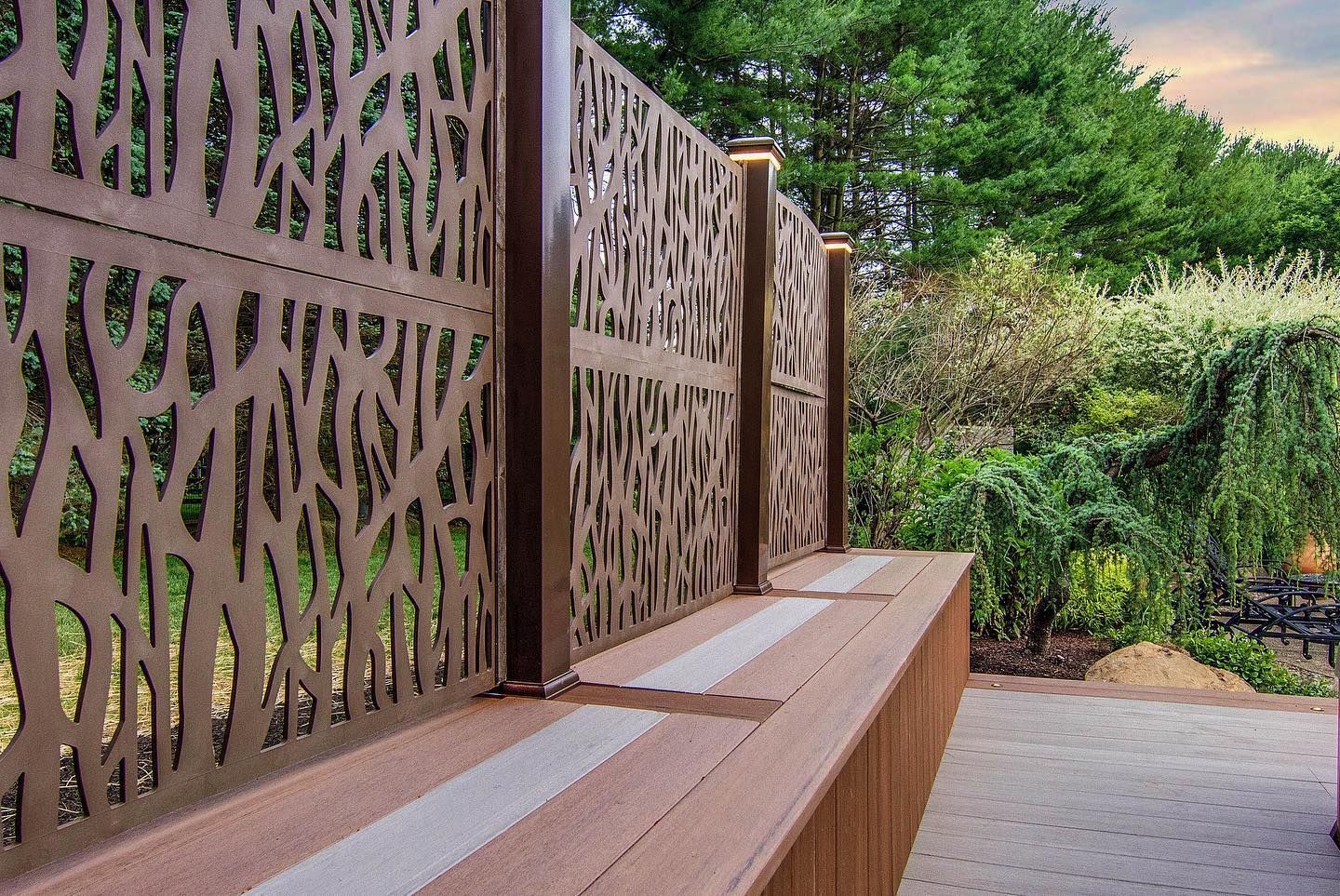 Brown metal screen fence with tree-like cutouts, built-in bench, and greenery in the background.