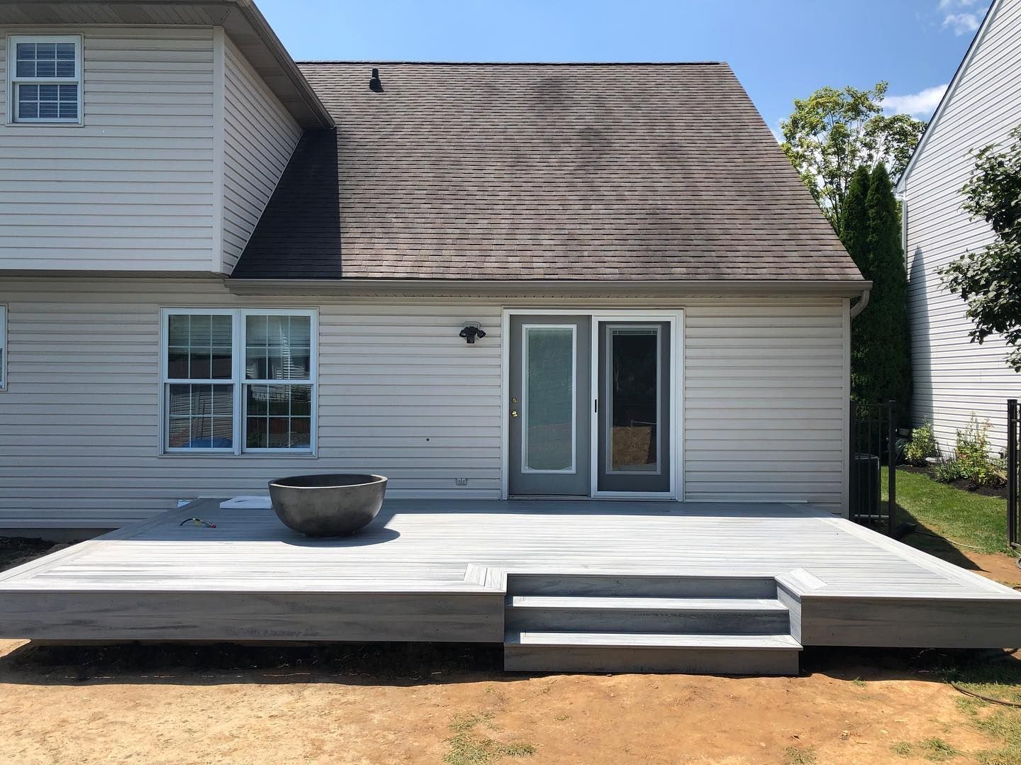 Backyard with composite deck, gray steps, sliding glass door, and house. Fire pit on deck.