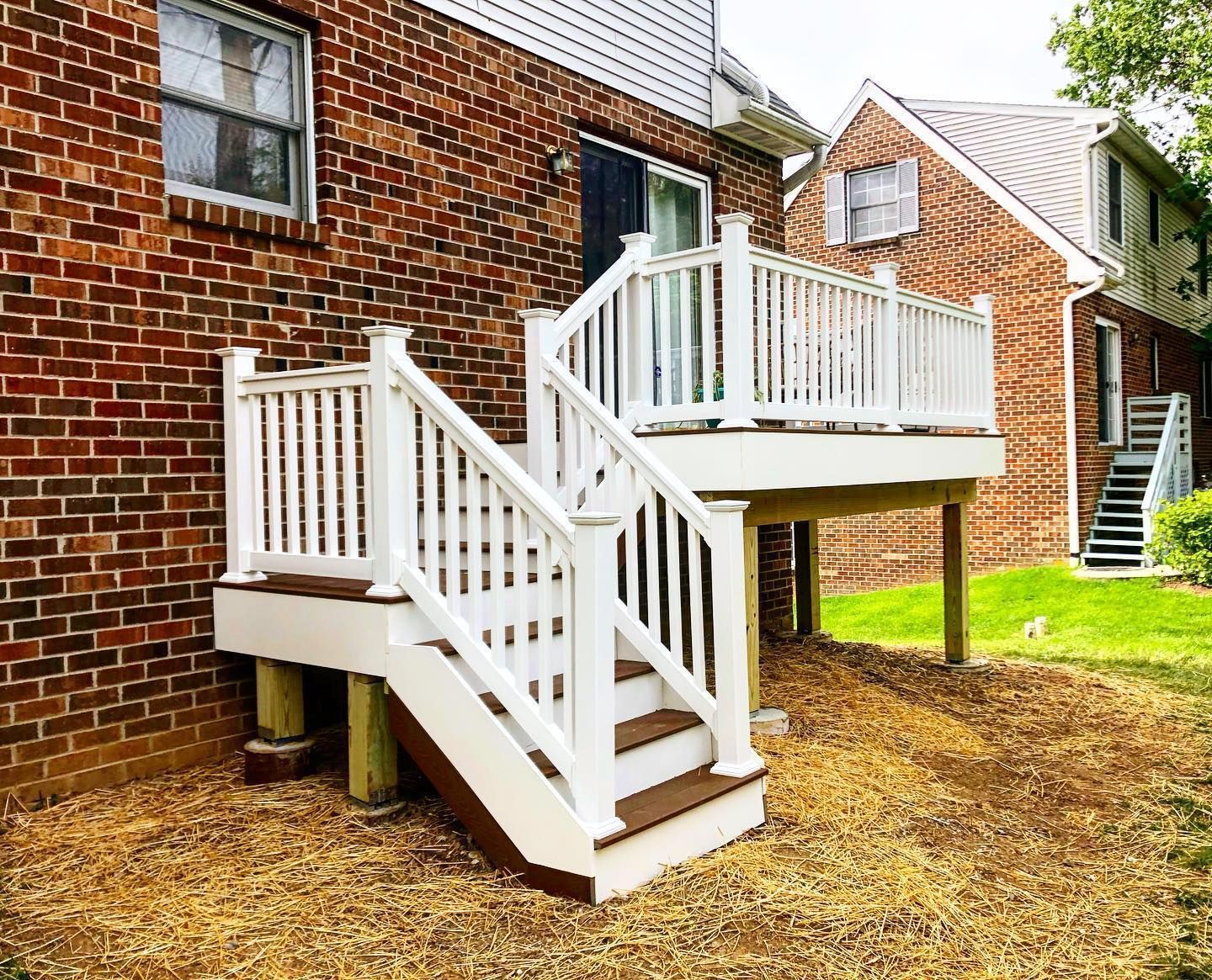 White deck with stairs against a brick building, second deck visible in the background.