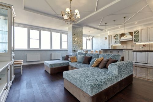 Spacious living room with sectional sofa, kitchen, and large windows; dark wood floors.