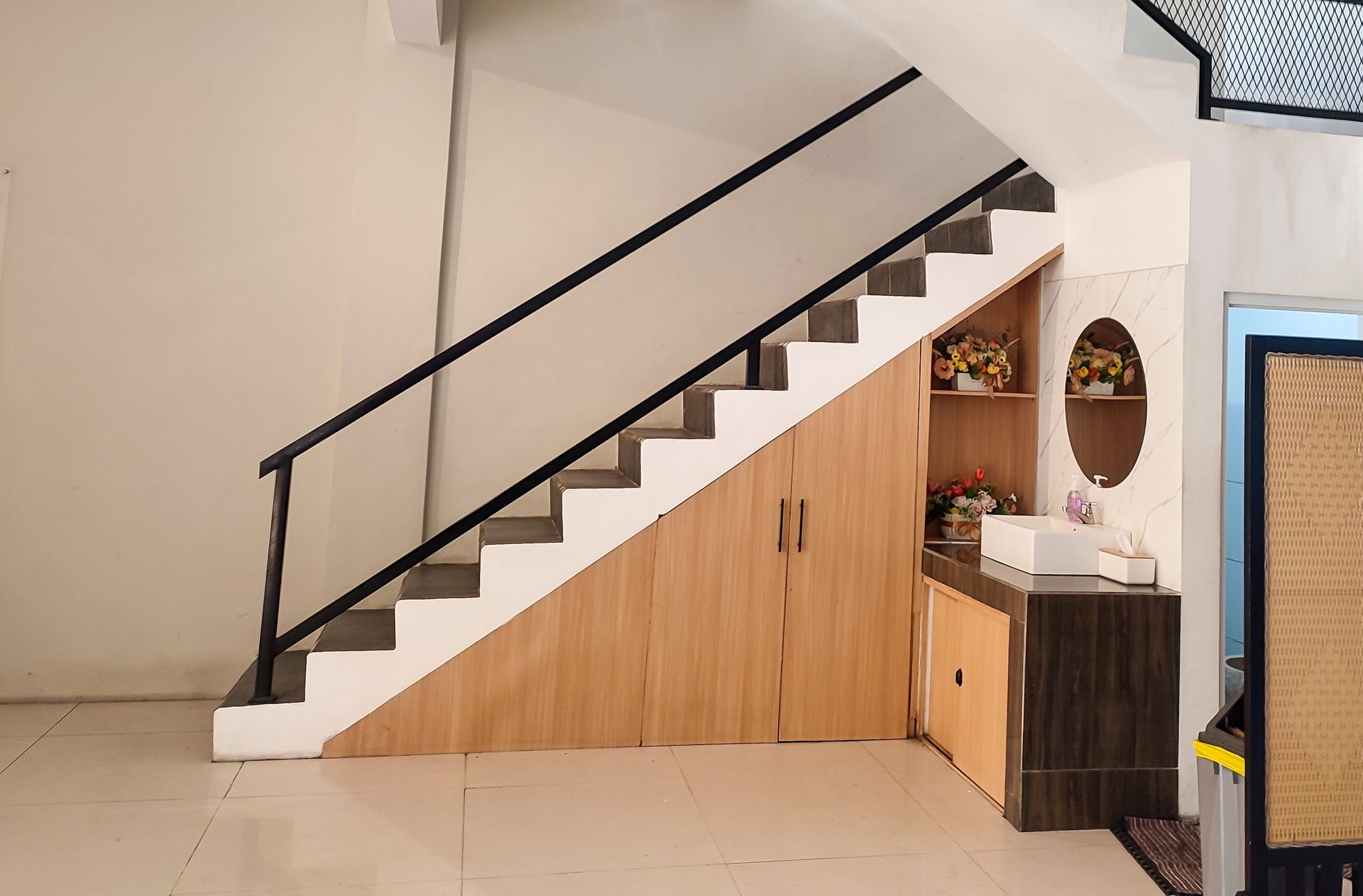 Staircase with black railing, white steps, wooden cabinet, and decorative items.