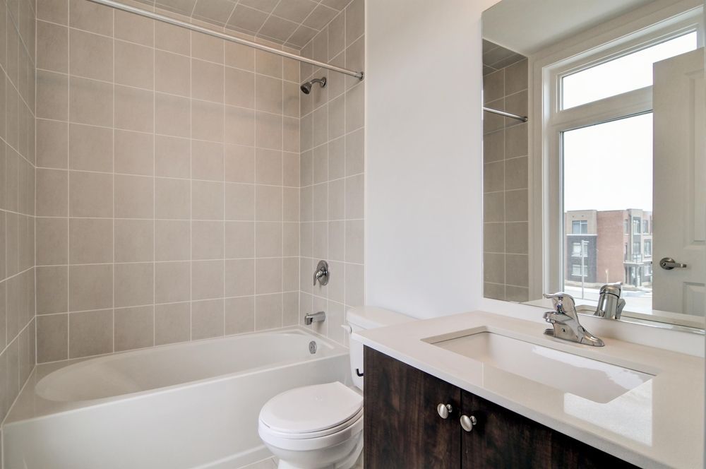 Bathroom with a white bathtub, toilet, and sink. Beige tile walls. Dark wood vanity. Window with outside view.