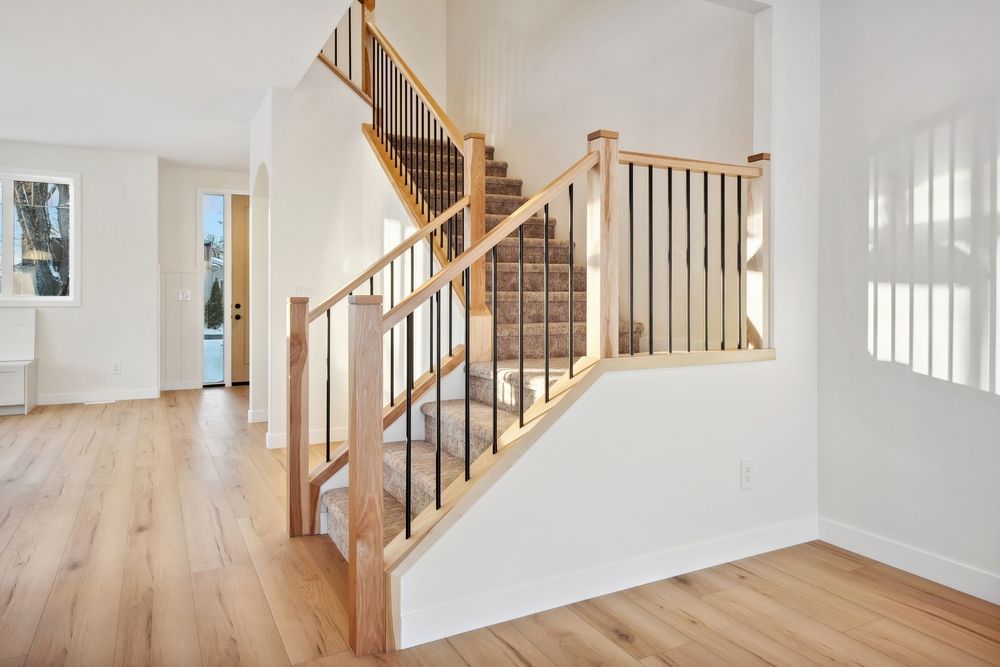 Wooden staircase with black metal balusters, carpeted steps, and light wood flooring.