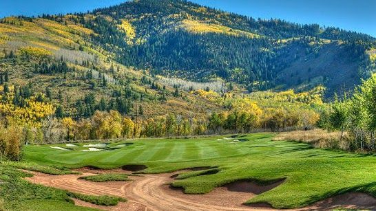 A golf course with mountains in the background and a dirt road in the foreground.