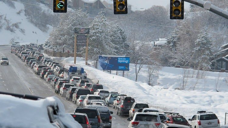 A long line of cars are driving down a snowy highway.