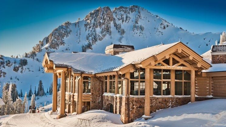 A large wooden house covered in snow with a mountain in the background.