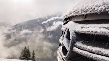 A close up of a car covered in snow with mountains in the background.