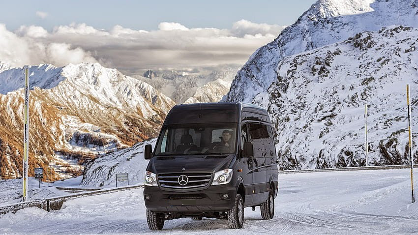 A black van is driving down a snowy mountain road.