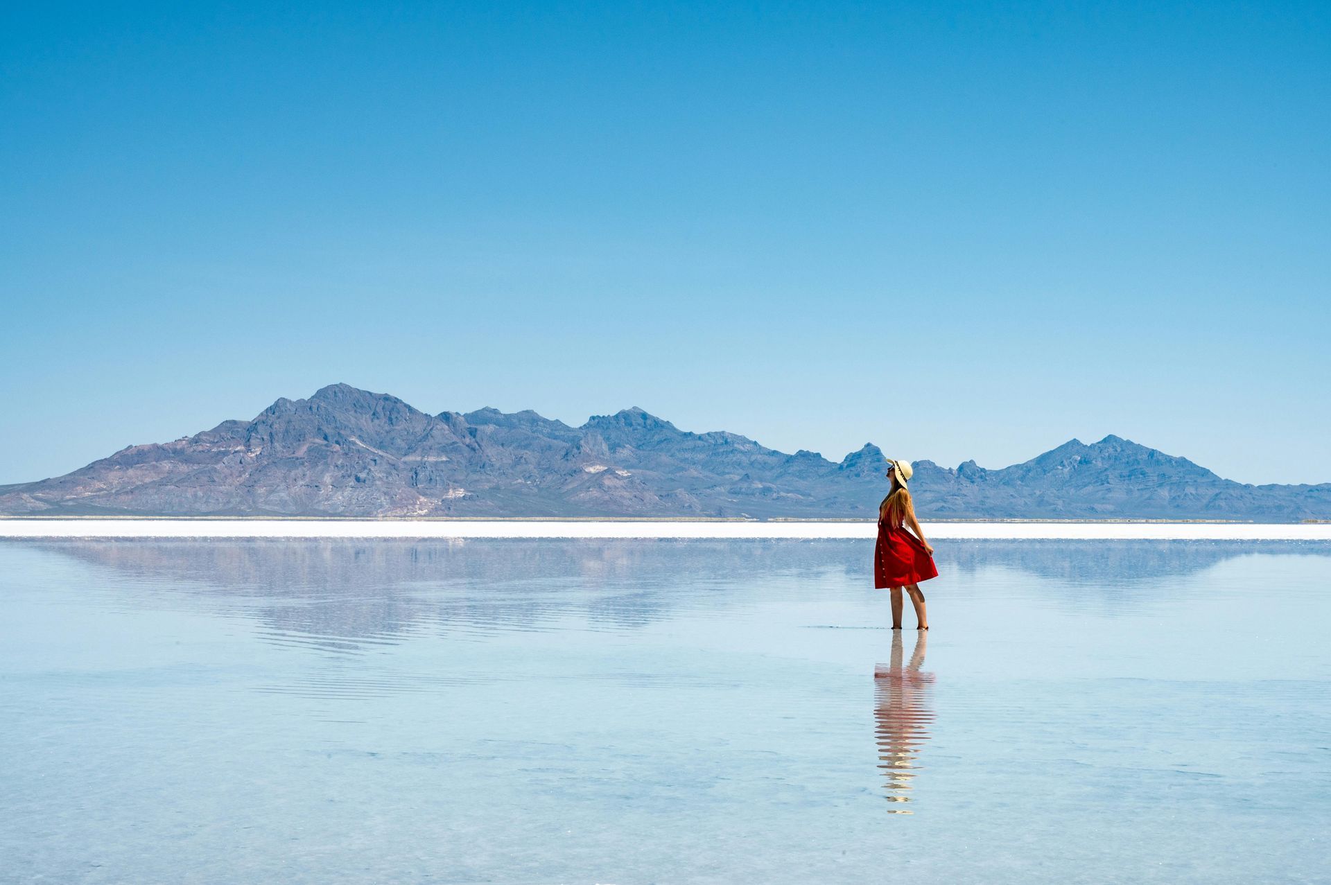 A woman in a red dress is standing in the middle of a lake.