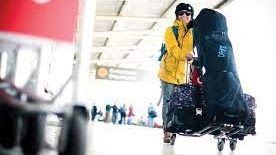 A man is carrying a snowboard on a cart at an airport.