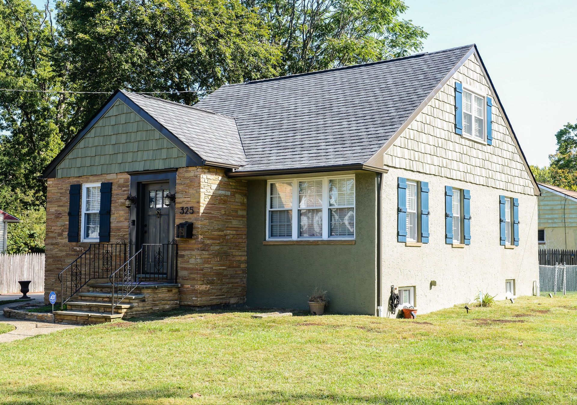 A one-story suburban house with a stone and stucco facade, a dark gray roof, and blue shutters on a sunny day.