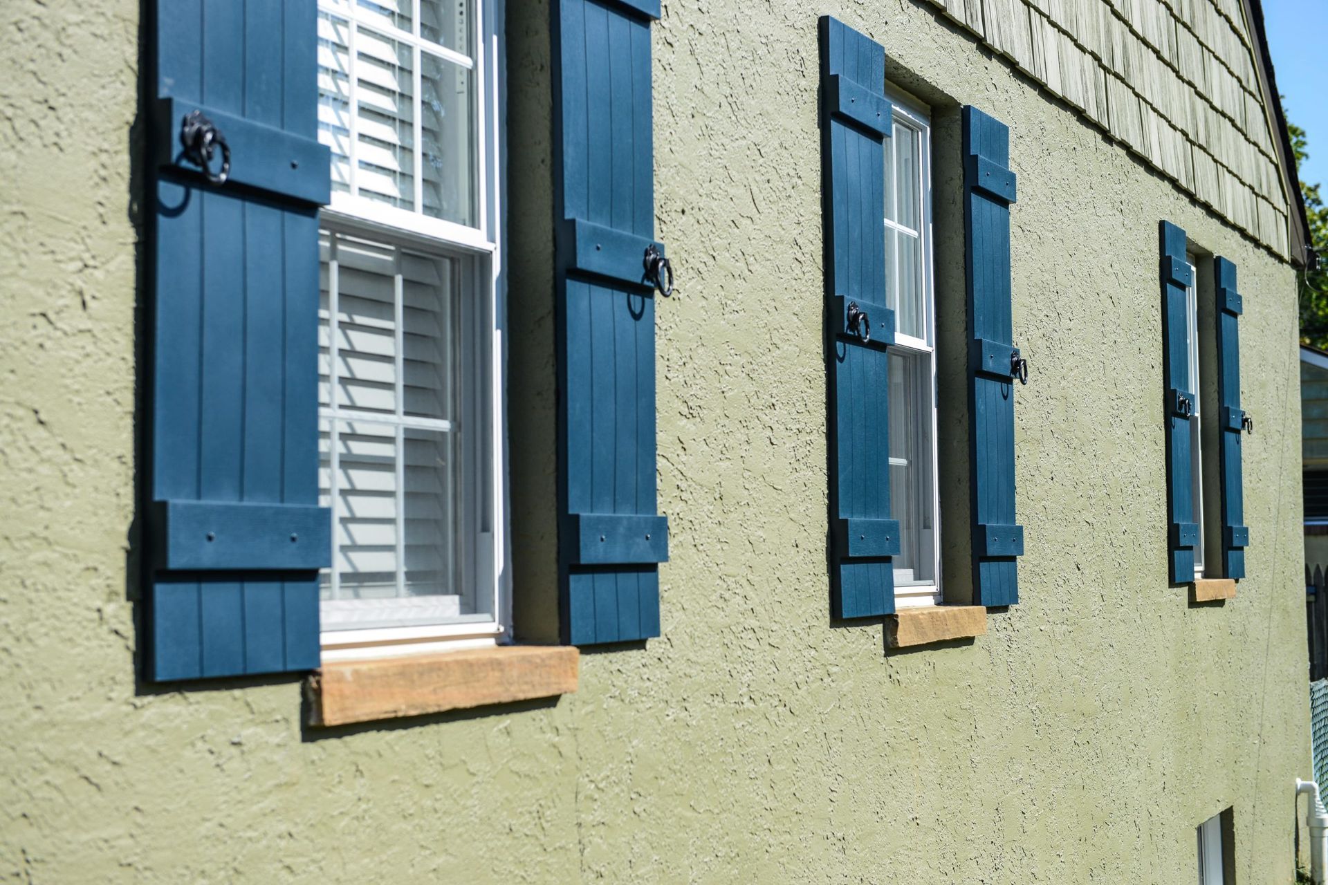 Three windows with blue wooden shutters on a light-colored, textured stucco wall.