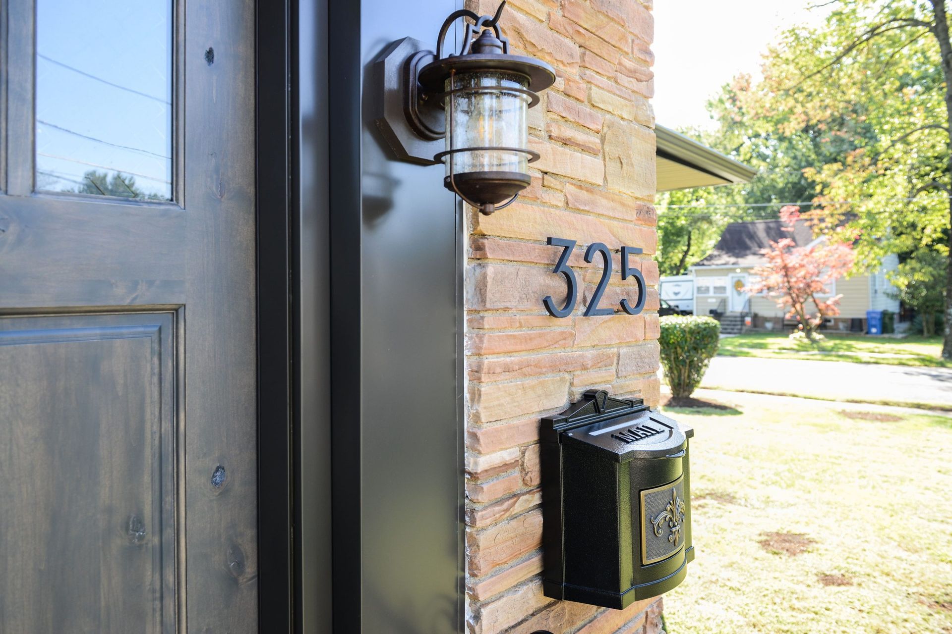 A brown wooden door next to a brick wall featuring a black wall-mounted mailbox and house number 325.